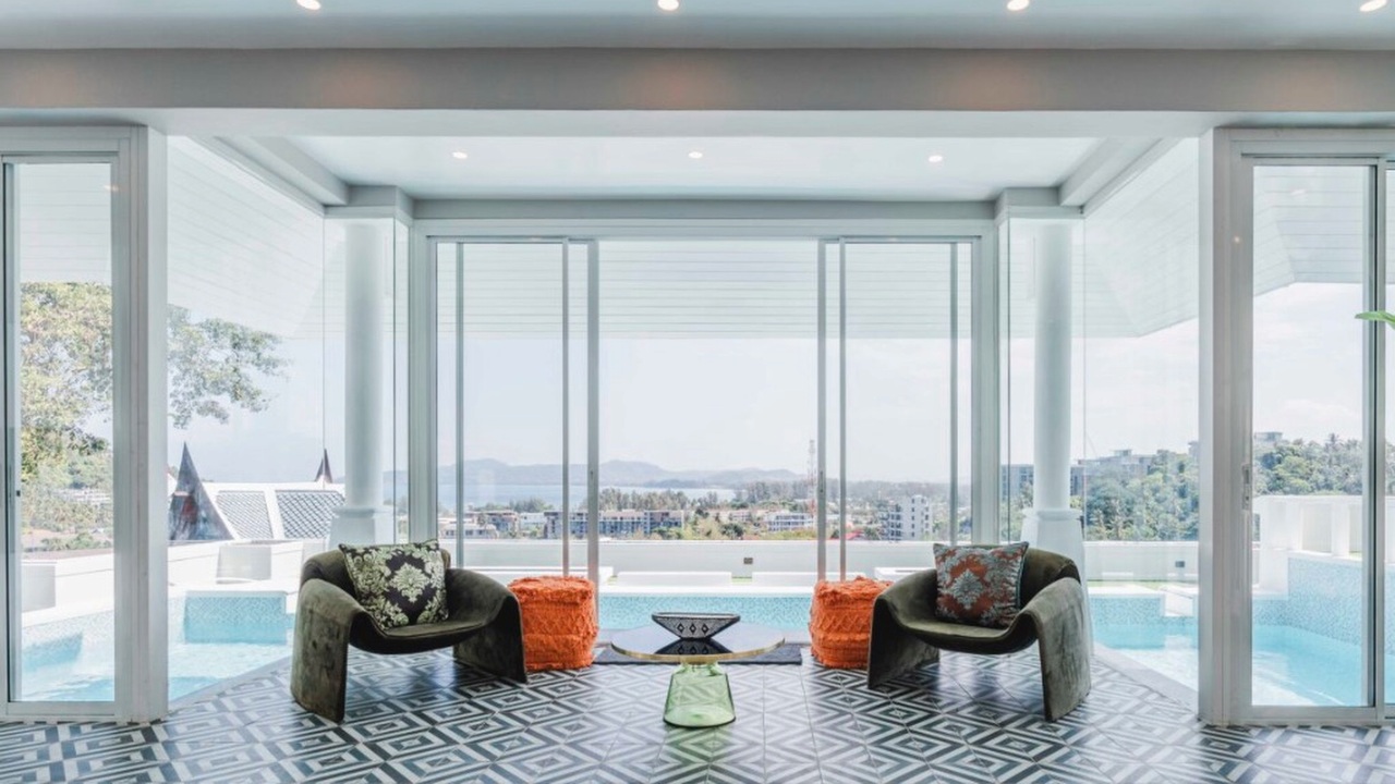 Glass viewing pavilion with velvet armchairs framing pool and sea views