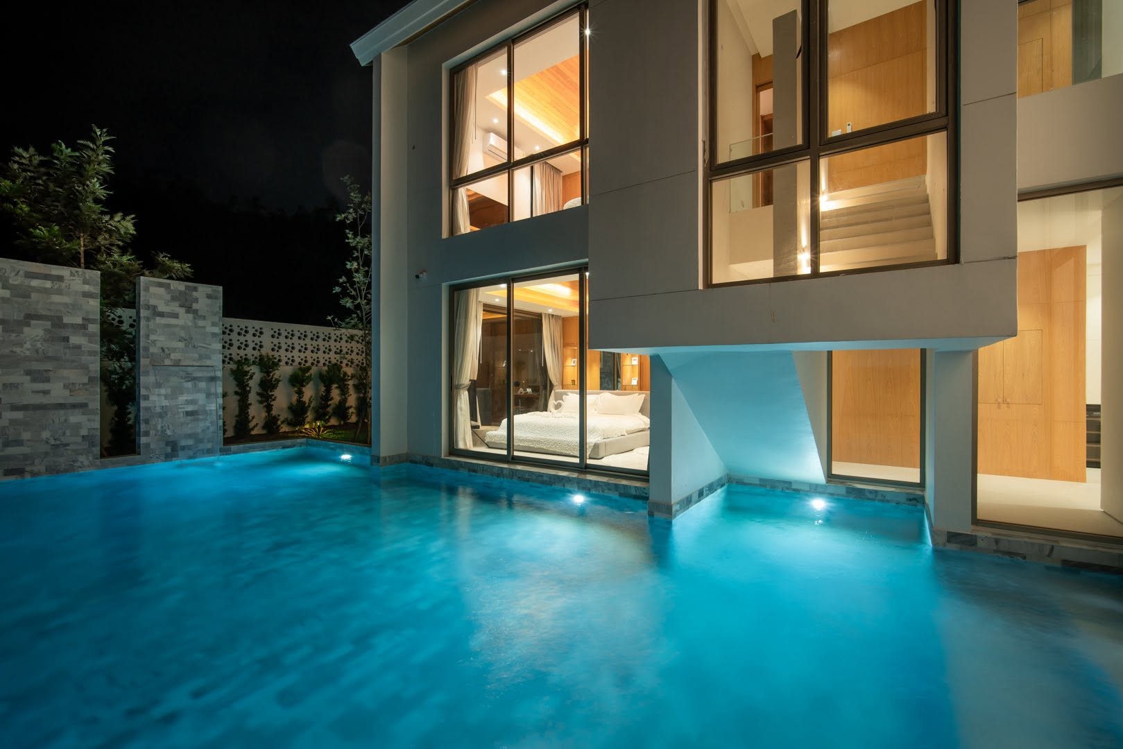 Illuminated pool at night with bedroom glow behind glass