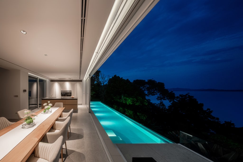 Open-plan dining and kitchen with illuminated pool at night
